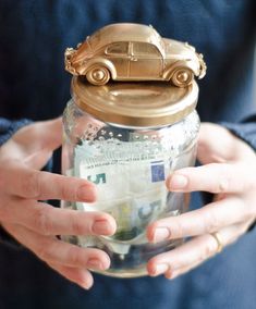 a person holding a jar filled with money and a toy car on top of it