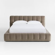 an upholstered bed with white sheets and pillows