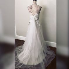 a white wedding dress is displayed on a mannequin stand in front of a wall