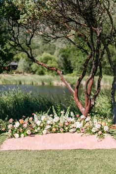 an outdoor ceremony setup with flowers and greenery on the grass near a lake, surrounded by trees