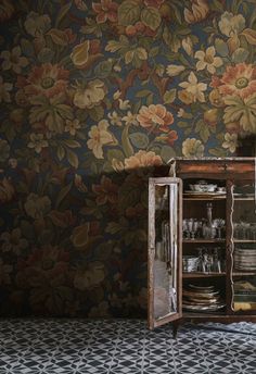 an old wooden cabinet in front of a floral wallpapered wall with plates and glasses on it