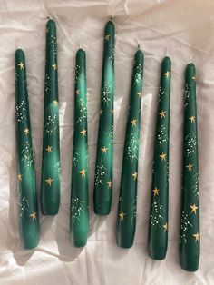 five green candles with gold stars on them sitting on a white sheeted surface,