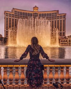 a woman standing in front of a fountain with her hands on the railing looking at the water