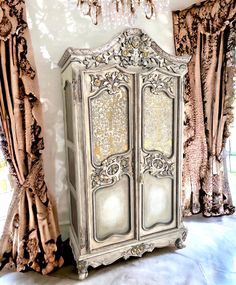 an ornate armoire in the corner of a room with drapes on the windows