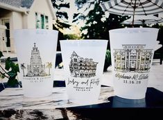 three plastic cups sitting on top of a wooden table next to an umbrella and building