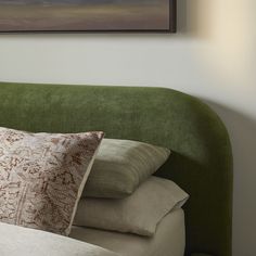 a green headboard with pillows on it and a painting hanging above the headboard