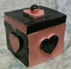 a small black and pink box with hearts on the top is sitting on a bed