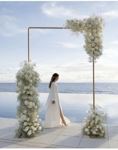 a woman standing in front of an outdoor ceremony arch with flowers and greenery on it