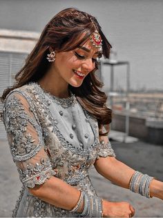 a woman in a silver dress holding something with both hands and smiling at the camera