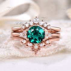 an emerald colored stone surrounded by white diamonds on top of a pink gold wedding ring