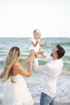 a man holding a baby up to his face while standing on the beach with two other people