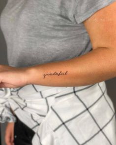 a woman with a small tattoo on her arm that says grateful in cursive writing