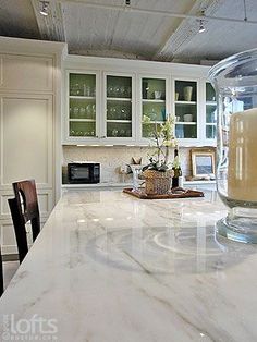 a kitchen with white cabinets and marble counter tops, along with a candle on the island