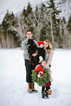 a family standing in the snow with a wreath on their chest and holding a dog