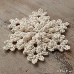 a crocheted snowflake laying on top of a wooden table