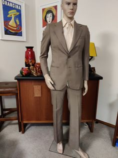 This is a suit designed by John Weitz in the 70s who originally started his career in womens fashion in the 50s swapping to menswear in the 60s. The suit is marked both terylene and polyester wool and mohair with a viscose lining. The taupe suit is in a multi season light weight fabric in a taupe brown, has medium wide lapels a two button closure and a single back vent. It is a slim fit antappered in at the waist. The pants are fitted through the hips and thighs with a slightly flared legs. Ther Tailored Retro Suits For Workwear, Retro Semi-formal Single-breasted Suits, Retro Fitted Single Breasted Blazer, Retro Single-breasted Semi-formal Suits, Fitted Brown Three-piece Suit For Office, Retro Suits With Notch Lapel For Workwear, Retro Notch Lapel Suits For Workwear, Vintage Tailored Suits For Business Casual, Tailored Vintage Suits For Business Casual