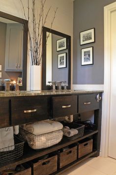 a bathroom vanity with drawers and baskets under the mirror, along with two framed pictures on the wall