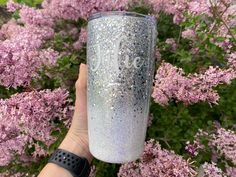 someone holding up a glitter tumbler in front of purple flowers