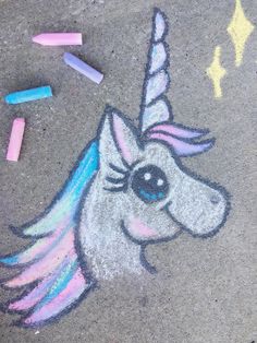 a chalk drawing of a unicorn with pastel crayons on the ground next to it