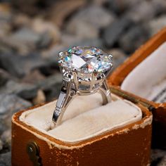 a diamond ring sits in an open box on the ground next to some rocks and stones