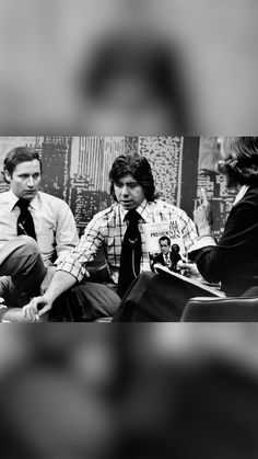 three men sitting on a bench in front of a wall and one is wearing a tie