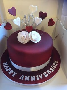 a red cake with white flowers and hearts on top is in a box that says 40 years anniversary