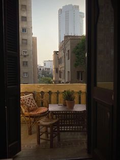 an open door leading to a balcony with chairs and tables on it in front of tall buildings