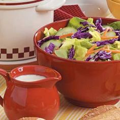 a red bowl filled with lettuce and carrots next to a cup of milk