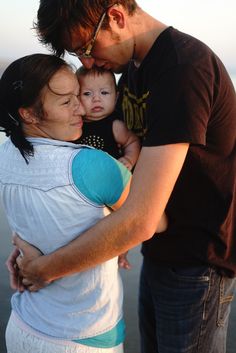 a man and woman holding a baby in their arms while standing next to the ocean