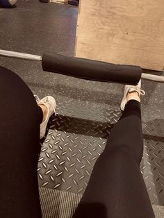 a person with black pants and white sneakers is sitting on a bench holding a barbell