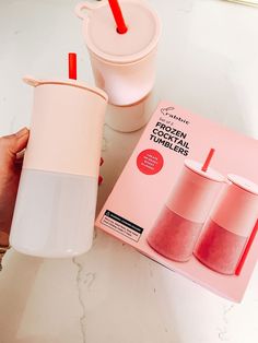 a person is holding two cups next to a pink box with red straws on it