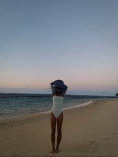 a woman standing on top of a sandy beach next to the ocean wearing a white bodysuit