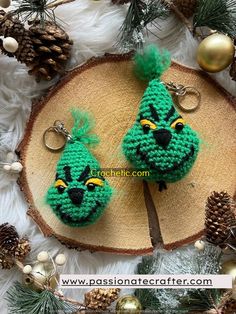 two crocheted keychains sitting on top of a piece of wood next to pine cones