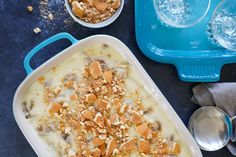 an ice cream dish with nuts in it next to two glasses and spoons on a table