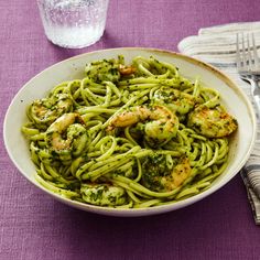 a bowl of pasta with shrimp and broccoli in it next to a glass of water