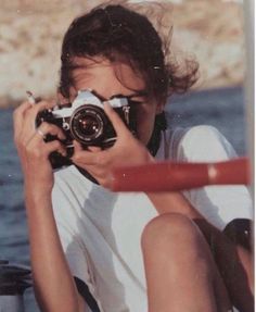 a woman holding a camera up to her face while sitting on a boat in the water