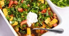 a casserole dish with vegetables and sour cream on the side, next to a salad