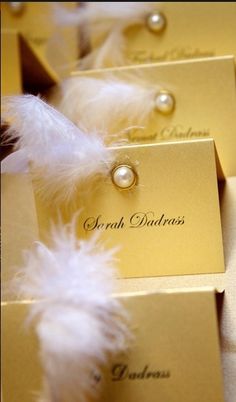 some white feathers are sitting on top of gold boxes with name tags attached to them