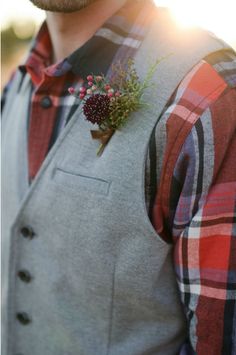 a man wearing a plaid shirt and vest with a flower in his lapel pocket