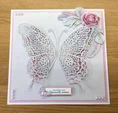 a card with a butterfly on it and a pink rose in the middle, sitting on a wooden table