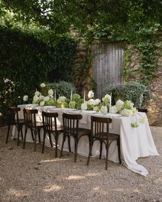 a table set up with white flowers and greenery for an outdoor wedding reception in the garden