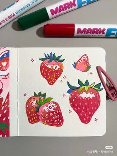 two markers are next to an open notebook with strawberries on it