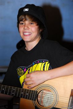 a young boy is smiling while holding an acoustic guitar and wearing a black beanie