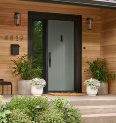 two planters with flowers are on the steps to a front door that is made of wood