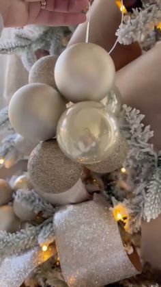 someone decorating a christmas tree with white and silver ornaments