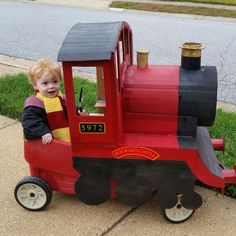 a toddler sitting in a toy train on the sidewalk