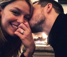 a man and woman kissing each other in front of a fire place with their hands together