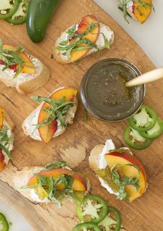 several small sandwiches are on a wooden cutting board with green peppers and sauce in the middle