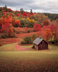 an old barn sits in the middle of a field surrounded by trees with fall colors