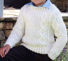 a young boy wearing a white sweater and blue bow tie sitting on a stone wall